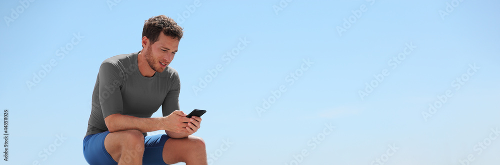 Happy man using phone app playing online game sitting outside after gym workout panoramic banner with sky background. Fitness athlete active lifestyle. Happy man using phone app playing online game sitting outside after gym workout panoramic banner with sky background. Fitness athlete active lifestyle.