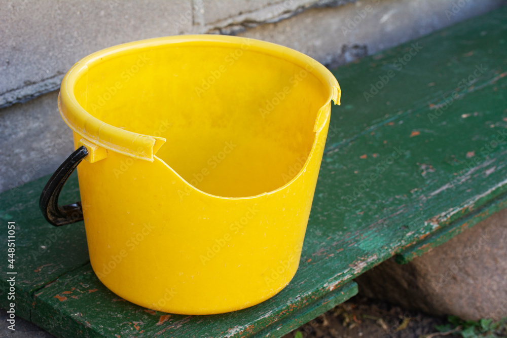 Empty dirty broken yellow plastic bucket on green bench.