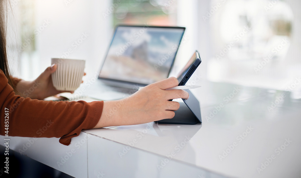 Focus on hand young asian woman holding stylus pen and using tablet working and blure other hand holding coffee cup while she working online with laptop in cafe Focus on hand young asian woman holding stylus pen and using tablet working and blure other hand holding coffee cup while she working online with laptop in cafe