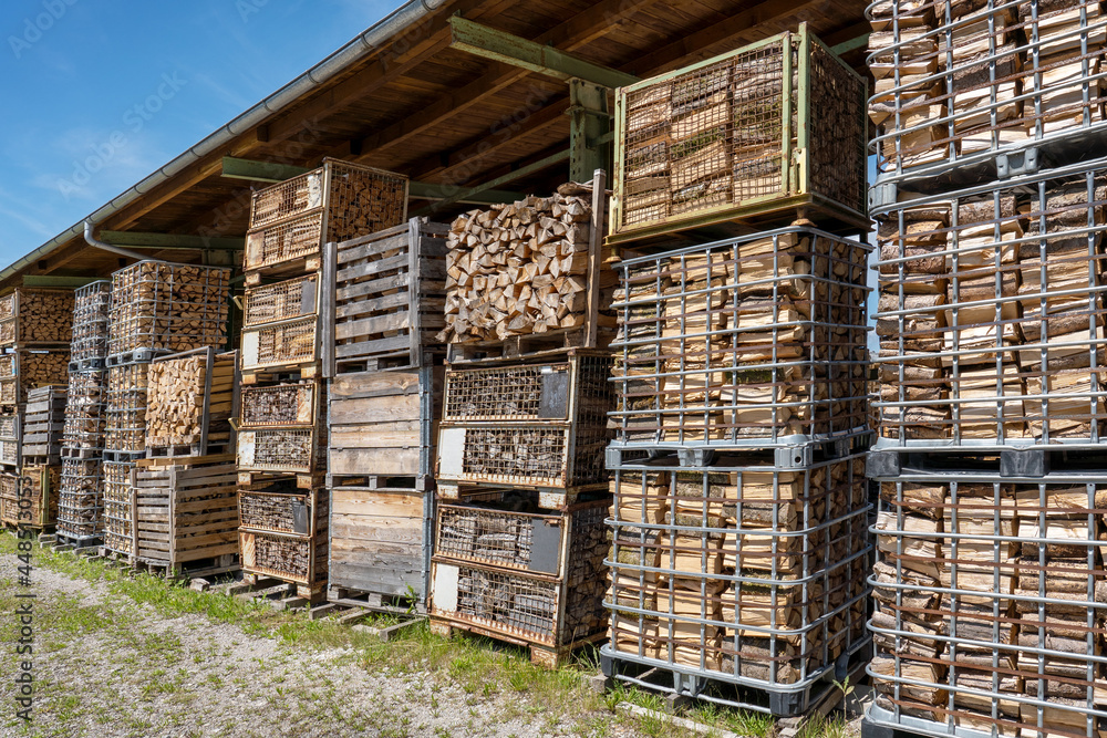 Brennholz in gestapelten alten Gitterboxen unter einem industriellen Dach im Freien Brennholz in gestapelten alten Gitterboxen unter einem industriellen Dach im Freien