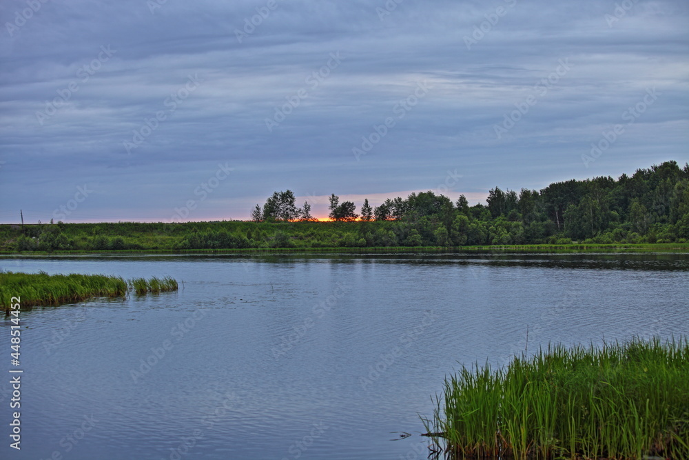 Beautiful orange sunset in the blue sky on the Volga River calm water with a forest on the horizon at summer evening, Russian natural landscape