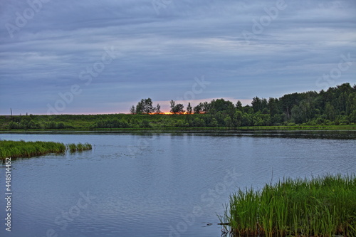 Beautiful orange sunset in the blue sky on the Volga River calm water with a forest on the horizon at summer evening, Russian natural landscape