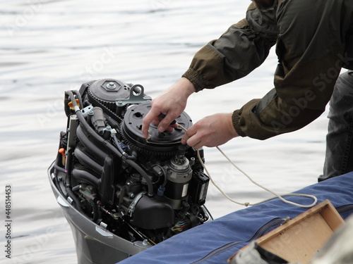 Boater hand start an broken outboard boat motor without the hood cap on the transom of the boat, emergency engine start with rope photo