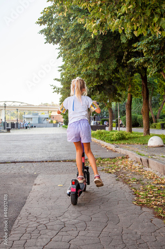 A girl of 8 years old rides an rented electric scooter in the park