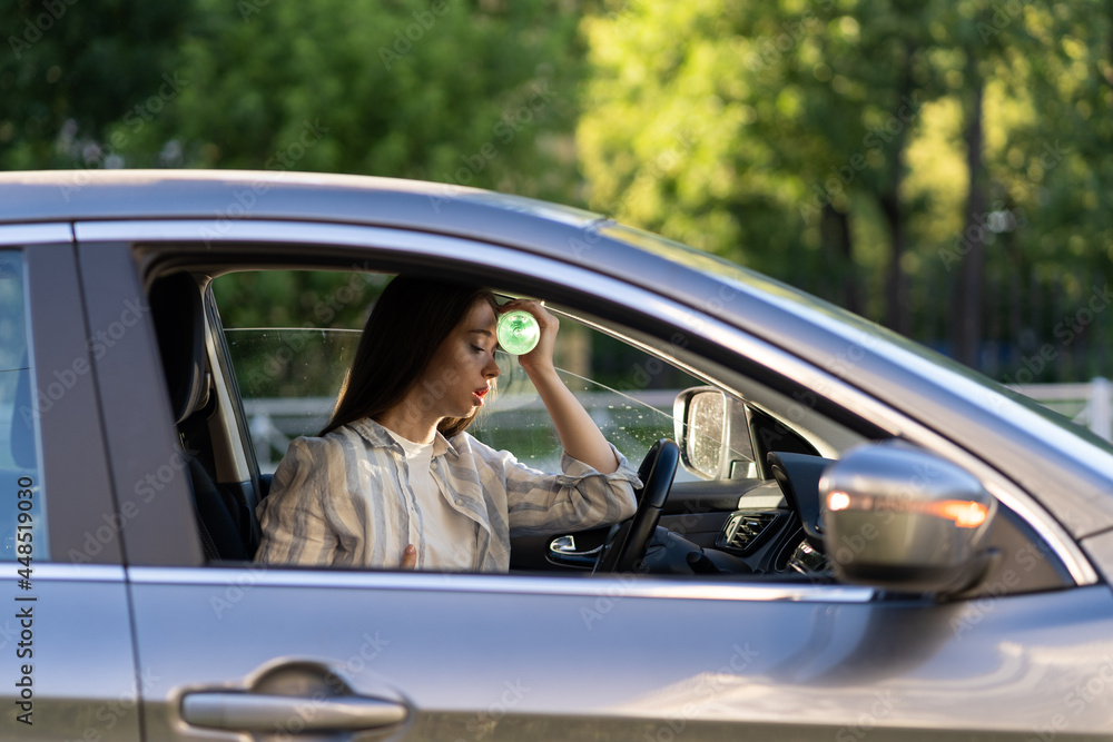 Exhausted woman driver feeling headache, sitting inside her car, applies bottle of water to forehead, hot weather. Tired girl stop after driving car in traffic jam. Blood pressure, heat concept. Exhausted woman driver feeling headache, sitting inside her car, applies bottle of water to forehead, hot weather. Tired girl stop after driving car in traffic jam. Blood pressure, heat concept.