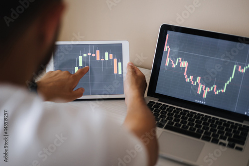 Young adult man trading on line with tablet pc connected to stock market. People, finance, investments. Over the shoulders