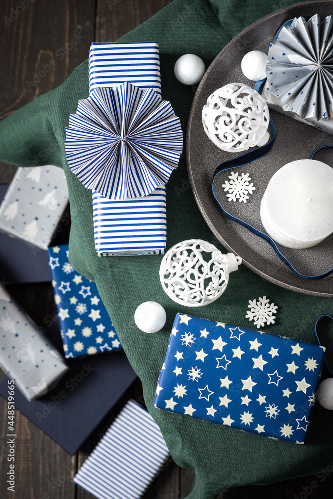 Obraz premium Christmas composition in white ,green and blue shades, Christmas balls and candle, gift boxes and snowflakes, decorative white spruce branches and snowball on a green tablecloth, top view