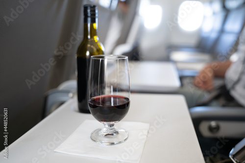 A glass with red wine and a small bottle in the background on the table of a passenger in an airplane photo