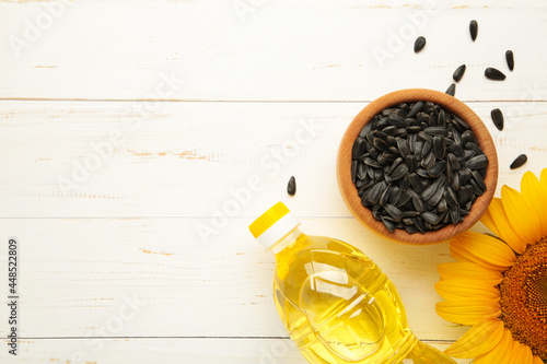 Sunflower oil, seed and sunflower on white wooden background photo