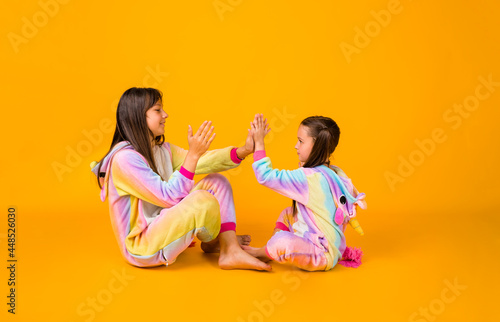 funny little girls in plush pajamas play on a yellow background with a copy of the space