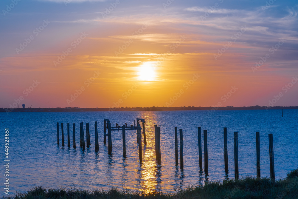View of a yellow sunset over Indian River, Florida from the A1A. Wooden pillars of the old pier near the coast as a typical view of Florida