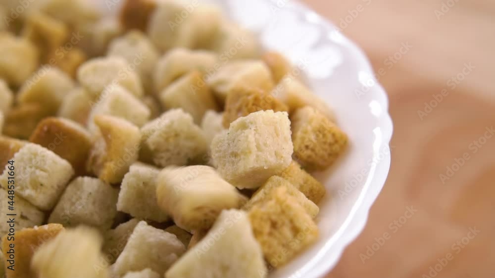 Fried bread croutons cubes fall in slow motion into a white bowl. Macro shot. On a wooden surface Fried bread croutons cubes fall in slow motion into a white bowl. Macro shot. On a wooden surface