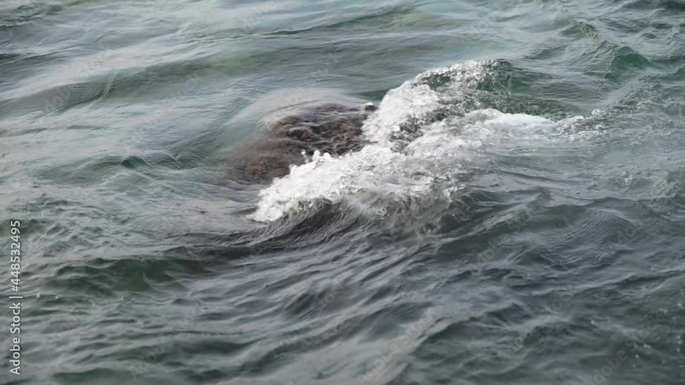 Slow motion of wave stream flowing through rocks. Close up of sea stone with flowing water, wave swell in a sea