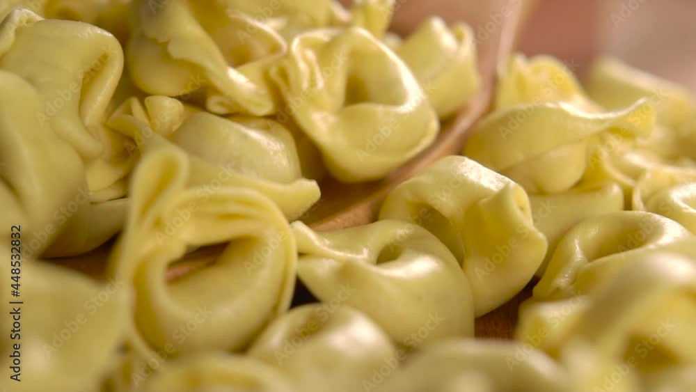 Raw dry Italian pasta tortellini in a full wooden spoon. Falling in slow motion. Macro shot Raw dry Italian pasta tortellini in a full wooden spoon. Falling in slow motion. Macro shot