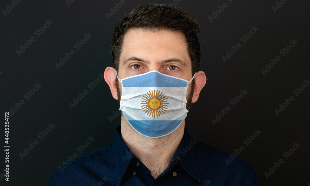 Man wearing Argentinian flag protective medical face mask. He looks worried and concerned. Coronavirus concept in Argentina with black background. Man wearing Argentinian flag protective medical face mask. He looks worried and concerned. Coronavirus concept in Argentina with black background.