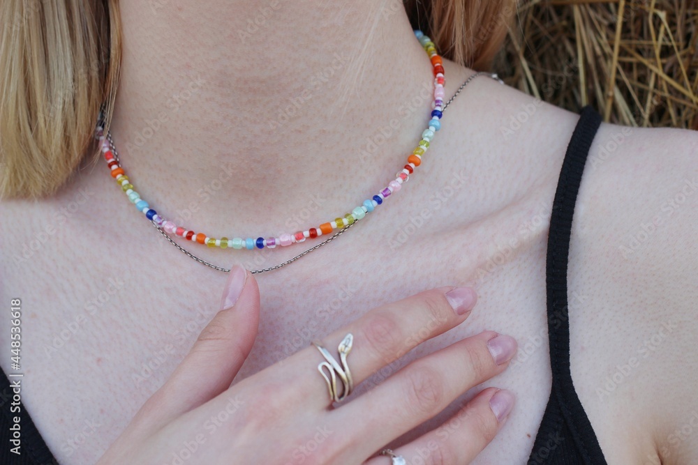 Body details of a beautiful young woman. Shoulder, collarbone and neck. A hand with rings touches the skin. Chain around the neck of multi-colored beads.