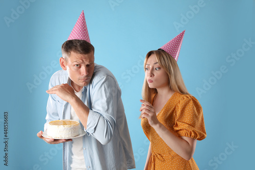 Greedy man hiding birthday cake from woman on turquoise background photo