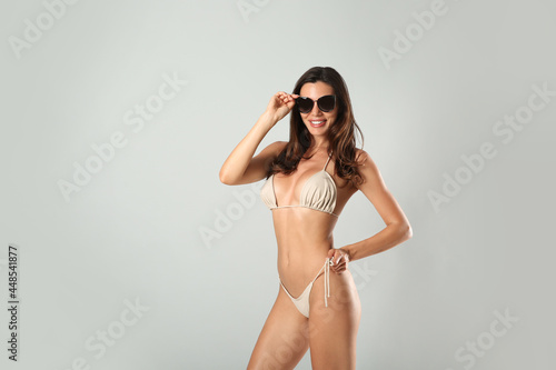 Beautiful woman in stylish bikini and sunglasses on light grey background. Space for text © New Africa