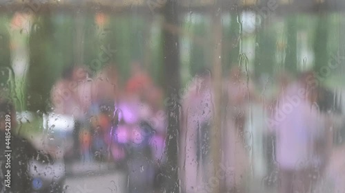 A window covered with rain, with a blurry bokeh background and raindrops running down the glass. Dancing people at a party outside the window in disfocus. photo