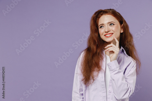 Fun young redhead curly woman 20s wears white T-shirt violet jacket look aside on workspace promo advert area isolated on pastel purple color wall background studio portrait. People emotions concept