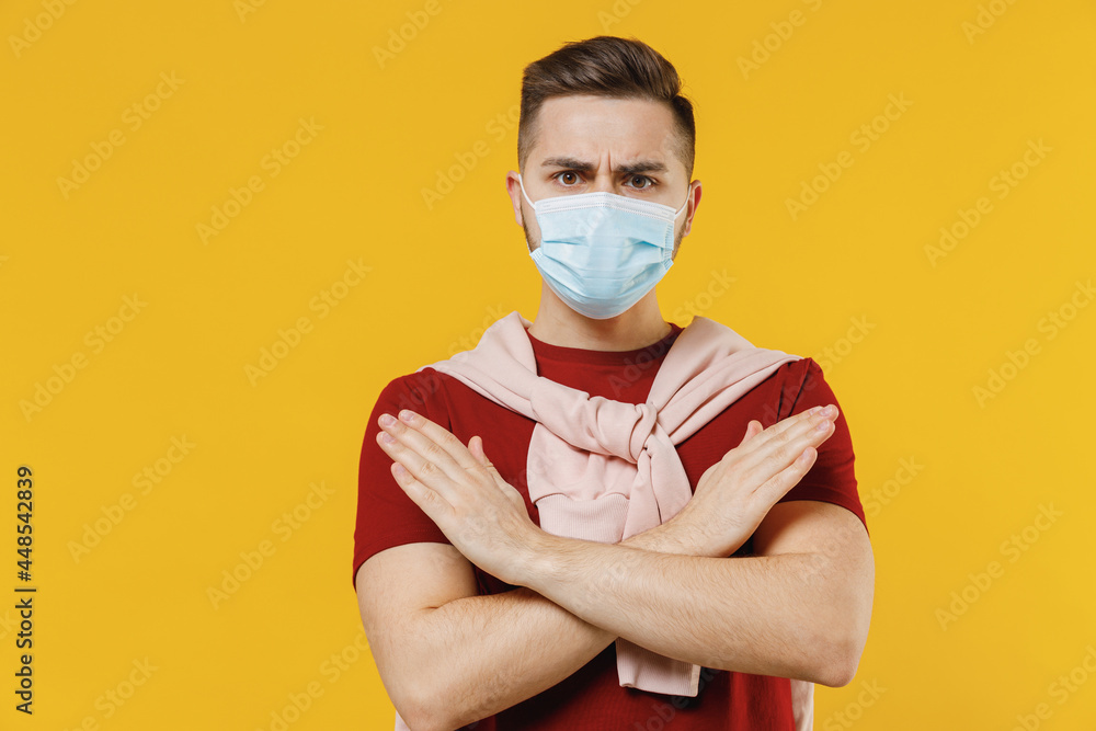 Young man in red t-shirt sterile face mask ppe to safe from coronavirus virus covid-19 flu on lockdown quarantine do stop crossed hand gesture isolated on plain yellow wall background studio portrait Young man in red t-shirt sterile face mask ppe to safe from coronavirus virus covid-19 flu on lockdown quarantine do stop crossed hand gesture isolated on plain yellow wall background studio portrait