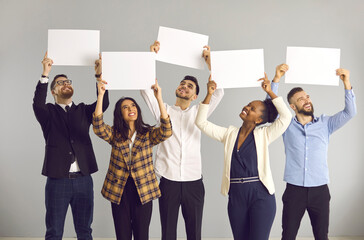 Group of five happy smiling people, office workers or friends, standing on gray background, holding white sheets of paper, empty signs, mockup banners, expressing opinion or giving positive feedback