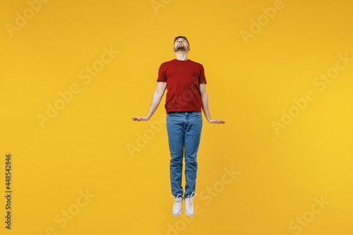 Full length cheerful happy young man wear red t-shirt casual clothes jump high clench fists do flying gesture isolated on plain yellow color wall background studio portrait. People lifestyle concept.
