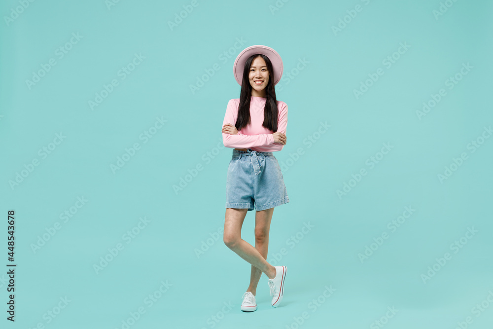 Full size body length happy cheerful fun young brunette asian woman 20s wear pink clothes holding folded crossed hands legs in stop gesture isolated on pastel blue color background studio portrait Full size body length happy cheerful fun young brunette asian woman 20s wear pink clothes holding folded crossed hands legs in stop gesture isolated on pastel blue color background studio portrait