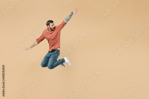 Full size body length surprised attractive happy tatooed young brunet man 20s short haircut wears apricot shirt jump like flying look aside back isolated on pastel orange background studio portrait