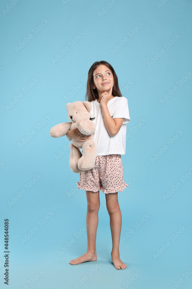 Cute girl wearing pajamas with teddy bear on light blue background Cute girl wearing pajamas with teddy bear on light blue background