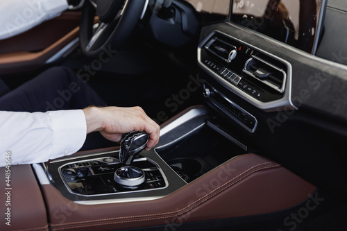 Close up cropped up photo shot hands european businessman man wearing white shirt sitting in car salon driving changes gears hold steering wheel automobile modern vehicle. Car sales driver concept