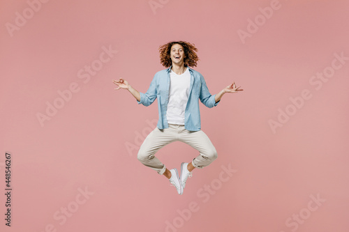 Full length young man 20s with long curly hair in casual clothes hold spread hand in yoga om aum gesture relax meditate try to calm down jump high isolated on pastel plain pink wall background studio