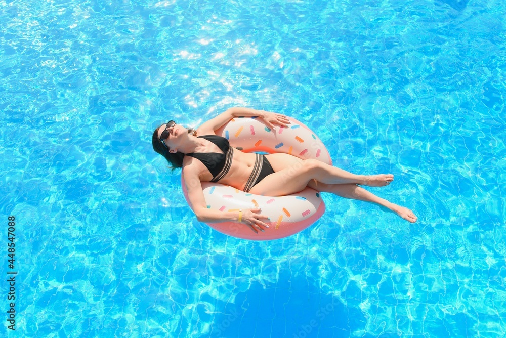 Beautiful woman and inflatable swim ring in shape of a donut in the pool