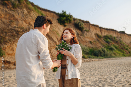 Young happy fun excited couple family man woman in white clothes rest relax together boyfriend meet girlfriend gift give bouquet flowers at sunrise over sea sand beach outdoor seaside in summer day.
