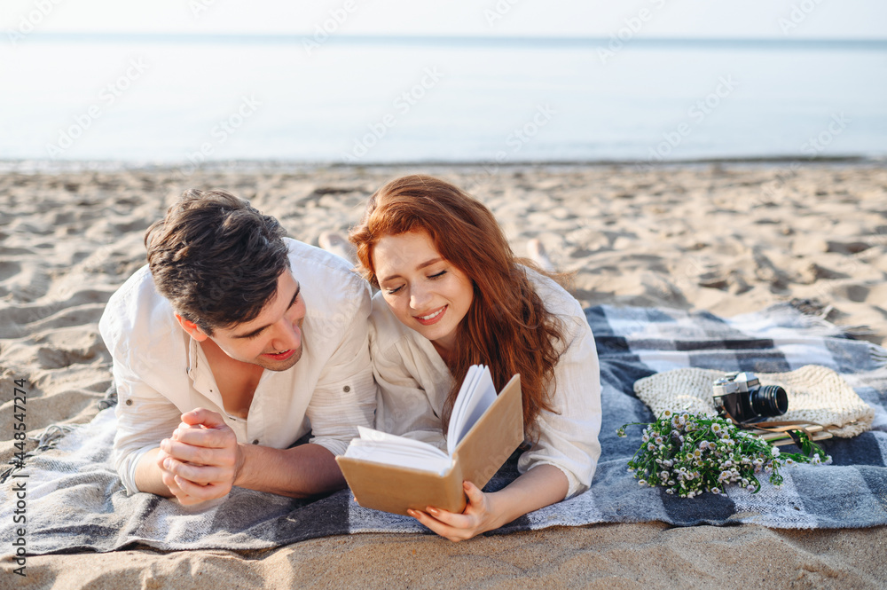 Happy young couple two family man woman in white clothes hug lying on picnic plaid reading book novel rest relax together at sunrise over sea beach ocean outdoor seaside in summer day sunset evening