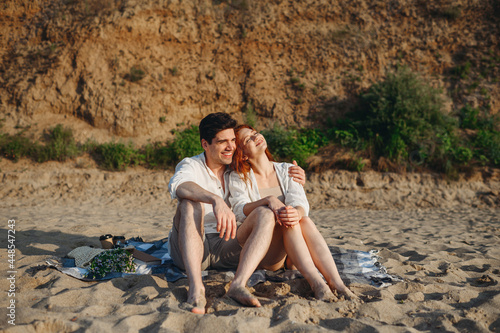 Full body happy smiling young couple two family man woman in white clothes hug sitting on picnic plaid rest relax together at sunrise over sea beach ocean outside seaside in summer day sunset evening