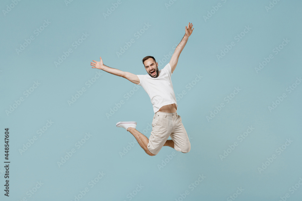 Full length young overjoyed fun joyful happy excited caucasian man 20s wear casual white t-shirt jump high with outstretched hands isolated on plain pastel light blue color background studio portrait