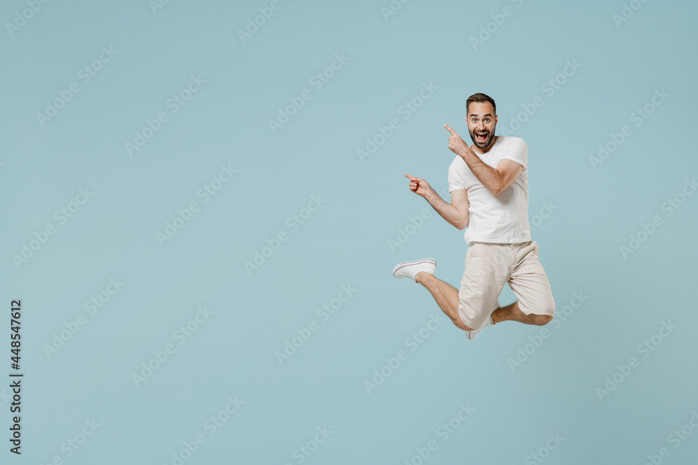 Full length young excited happy man 20s wearing casual white t-shirt jump high point index finger aside on workspace area mock up isolated on plain pastel light blue color background studio portrait Full length young excited happy man 20s wearing casual white t-shirt jump high point index finger aside on workspace area mock up isolated on plain pastel light blue color background studio portrait