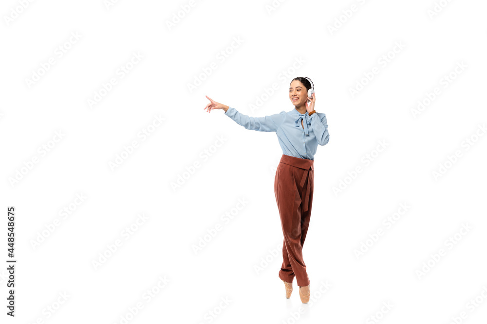 Obraz premium Smiling ballerina in headphones pointing with finger isolated on white