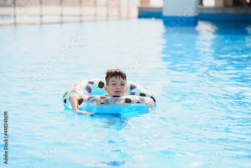 Happy boy in swimming pool. Boy is alone  swimming inflatable ring and surronded by water splashes. Wet teenager is enjoying summer weekend in amusement water park. Banner with copy space