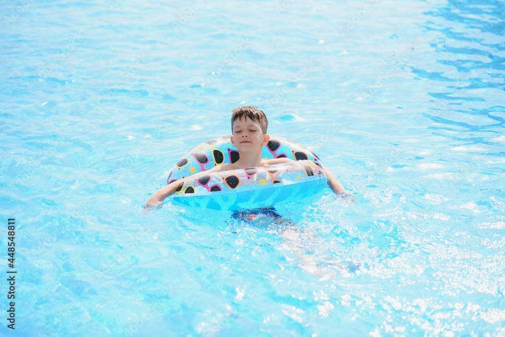 Happy boy in swimming pool. Boy is alone, swimming inflatable ring and surronded by water splashes. Wet teenager is enjoying summer weekend in amusement water park. Banner with copy space