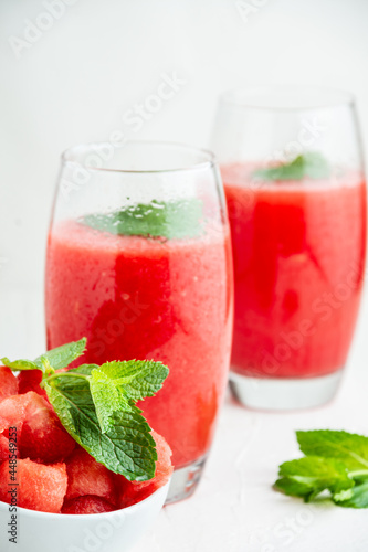 Top view of two glasses with watermelon juice, mint, and bowl with pieces of watermelon, selective focus, on table and white background, in vertical