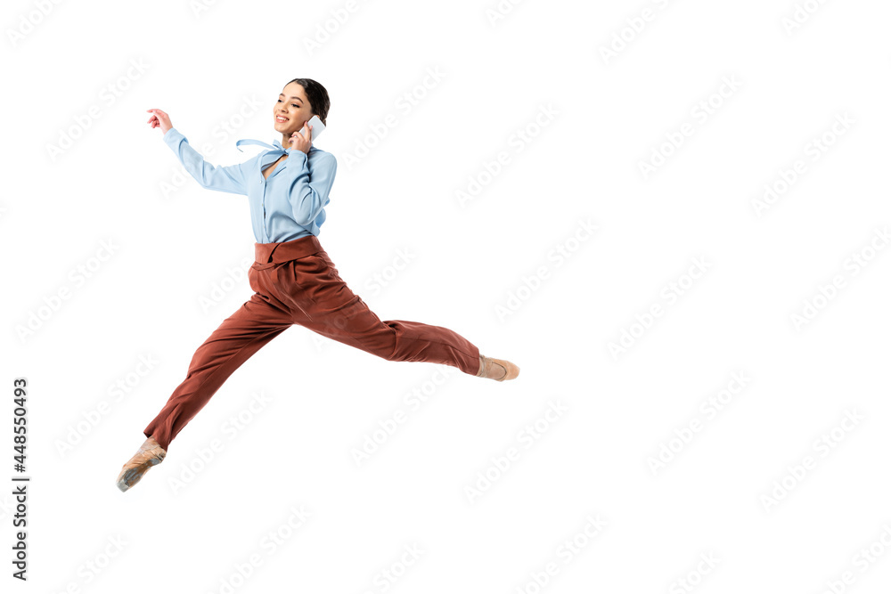 Smiling ballerina talking on smartphone while jumping isolated on white