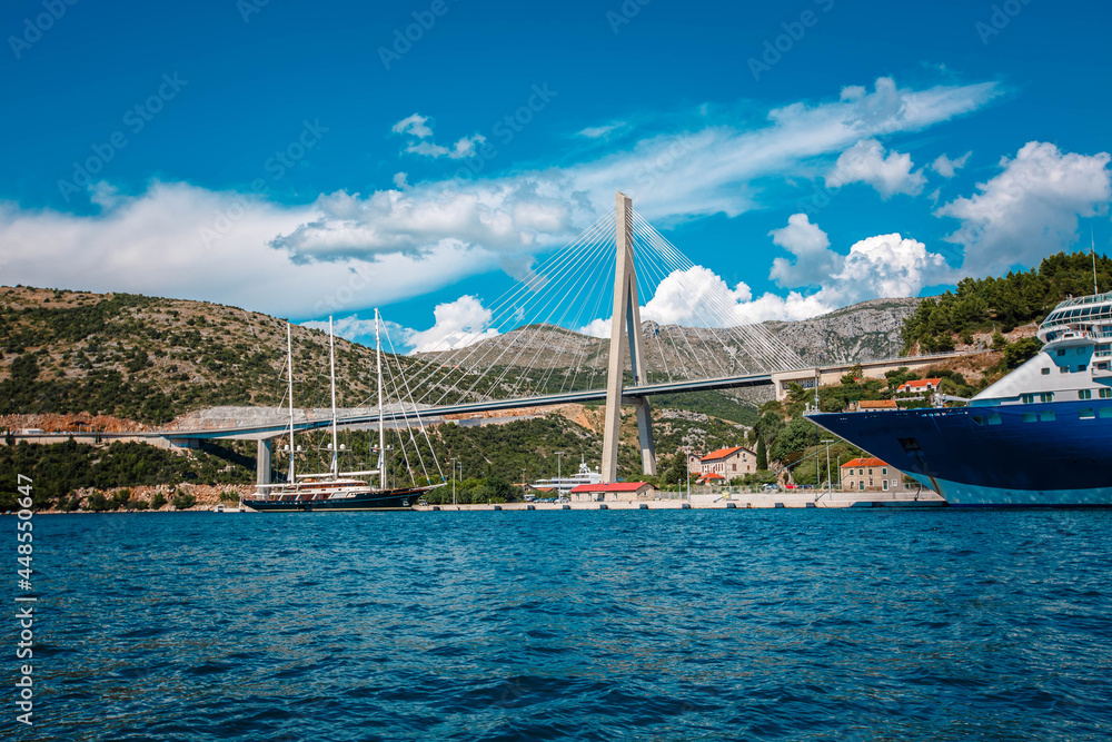Port in Dubrovnik, Croatia. Summer landscape with road, bridge, boat, harbor, city, mountains, blue sea. Luxury cruise. View from the water to the floating liner