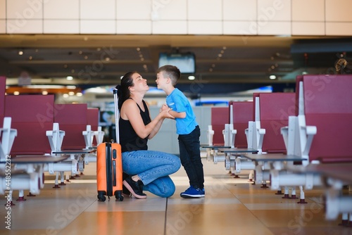 Family at airport before flight. Mother and son waiting to board at departure gate of modern international terminal. Traveling and flying with children. Mom with baby and toddler boarding airplane.