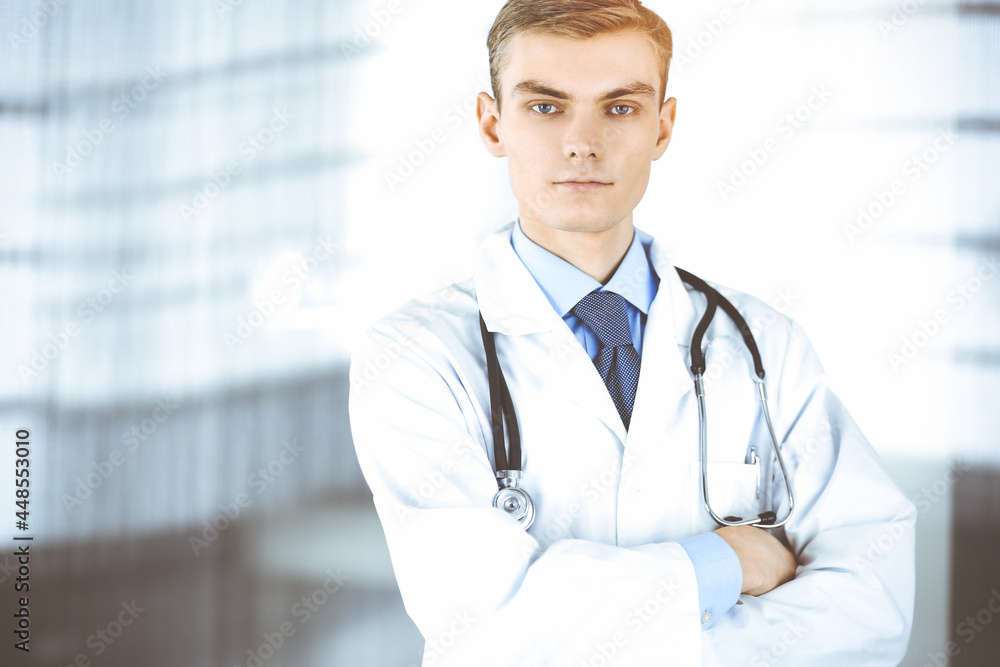 Doctor man, with a stethoscope, stands at his sunny hospital office. Perfect medical service in clinic. Happy future in medicine and healthcare Doctor man, with a stethoscope, stands at his sunny hospital office. Perfect medical service in clinic. Happy future in medicine and healthcare