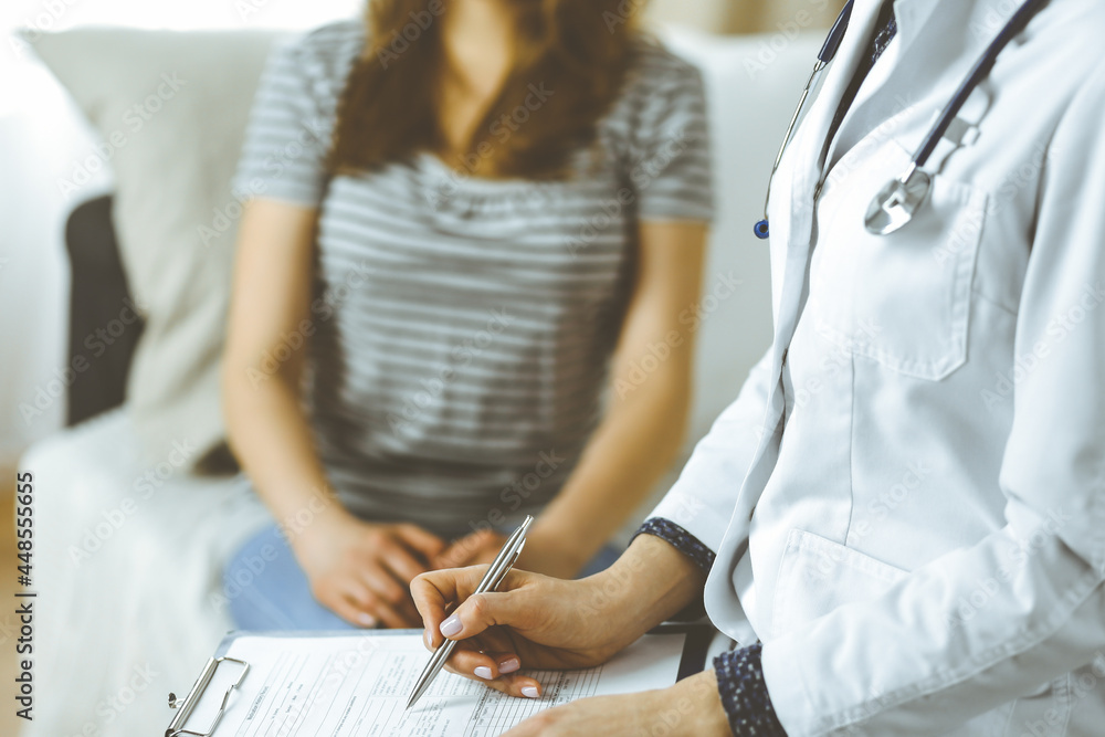 Obraz premium Unknown woman doctor and patient discussing current health examination while sitting in cozy living room. Stay at home concept during Coronavirus pandemic and self isolation quarantine