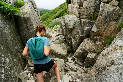 Backpacker female climbing on high natural mountain surrounded by natural wild scenery