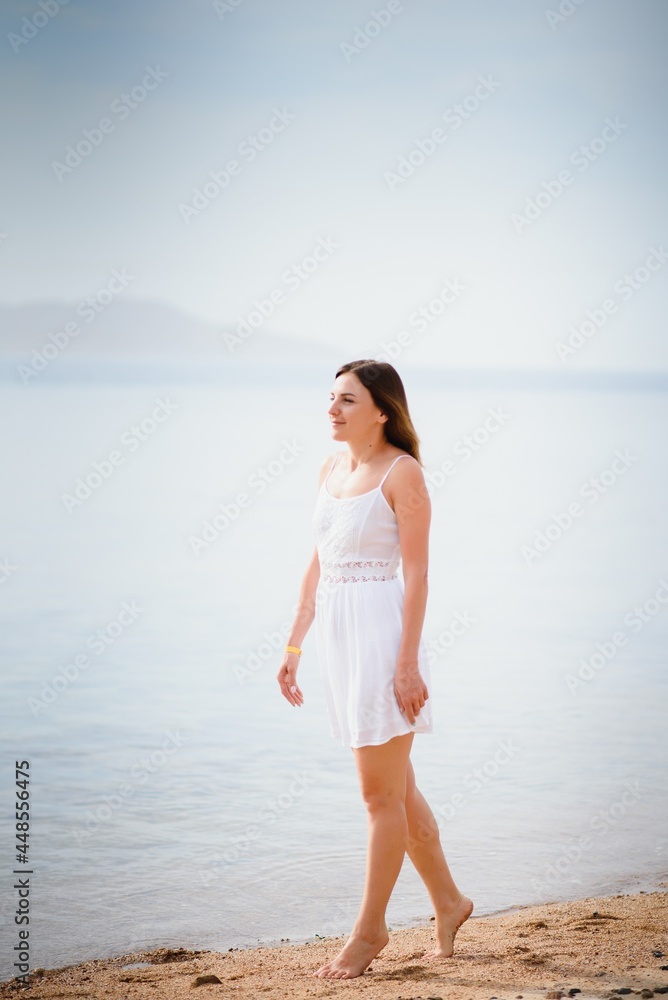 Beautiful woman in a white dress walking on the beach.Relaxed woman breathing fresh air,emotional sensual woman near the sea, enjoying summer.Travel and vacation. Freedom and inspiration concept Beautiful woman in a white dress walking on the beach.Relaxed woman breathing fresh air,emotional sensual woman near the sea, enjoying summer.Travel and vacation. Freedom and inspiration concept