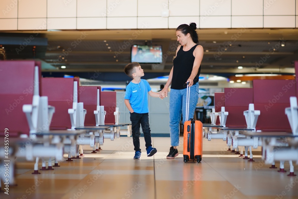 Family at airport before flight. Mother and son waiting to board at departure gate of modern international terminal. Traveling and flying with children. Mom with baby and toddler boarding airplane.